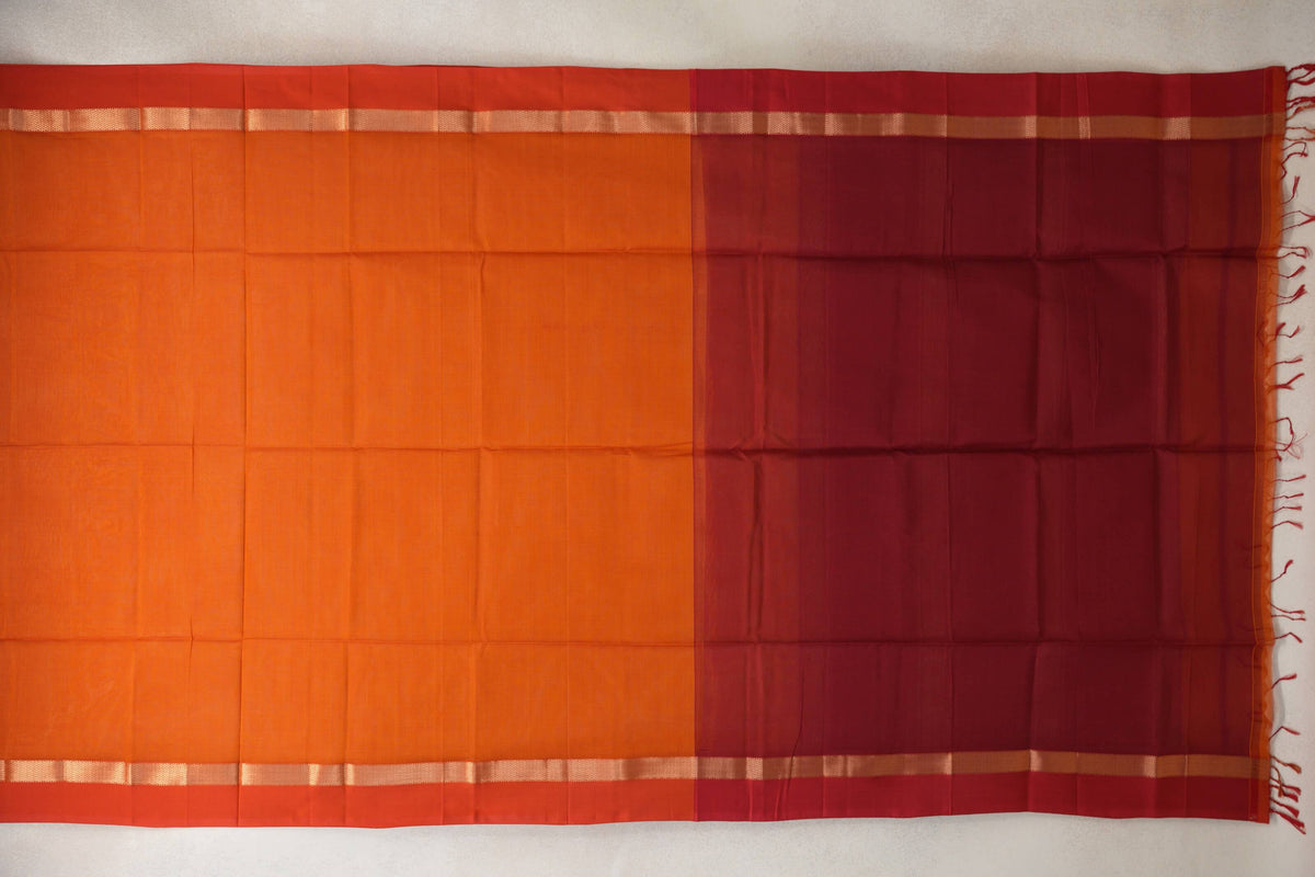 Maheshwari silk cotton saree laid flat, showing a reddish orange body, orangish red borders with narrow patterned bands, and a fringed reddish maroon pallu.