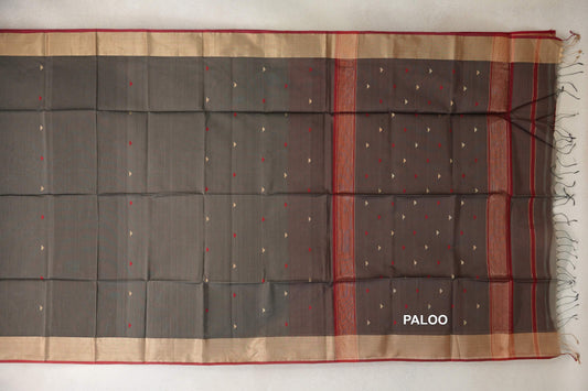 Maheshwari silk cotton saree laid flat, with a charcoal grey body, small red and cream triangles, beige borders with deep red edges, and a tasselled pallu.