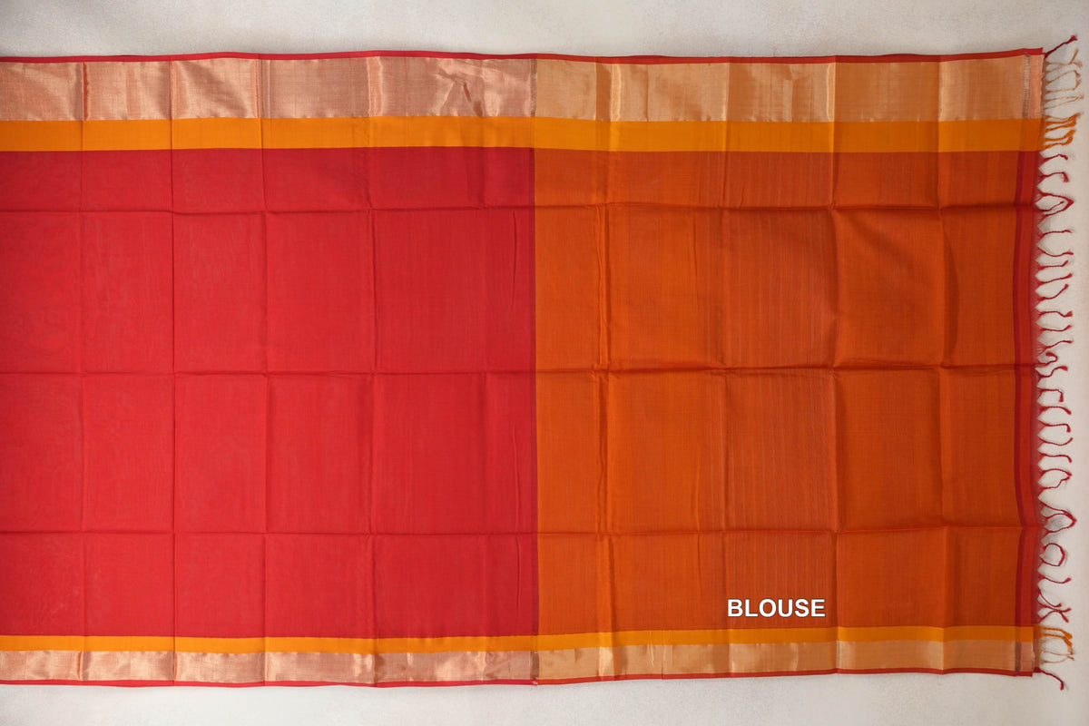 Maheshwari silk cotton saree laid flat, with a tomato red body, deep orange blouse piece, pale borders edged in red, and tassels at one end.