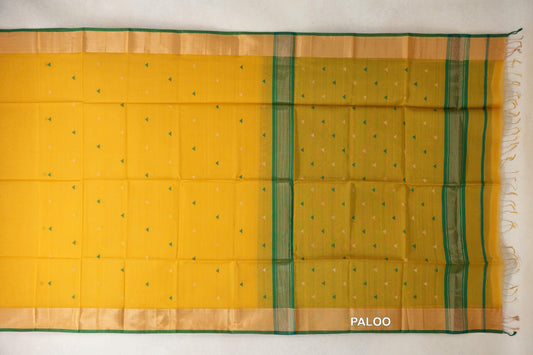 Maheshwari silk cotton saree laid flat, with a turmeric yellow body, scattered green and cream triangles, green-edged borders and a striped, fringed pallu.