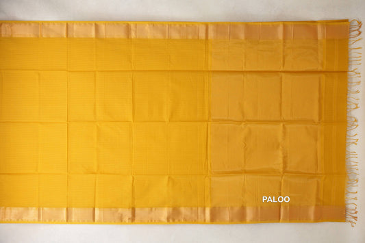 Turmeric yellow Maheshwari silk cotton saree laid flat, with a plain body, lustrous borders and a pallu ending in tassels.