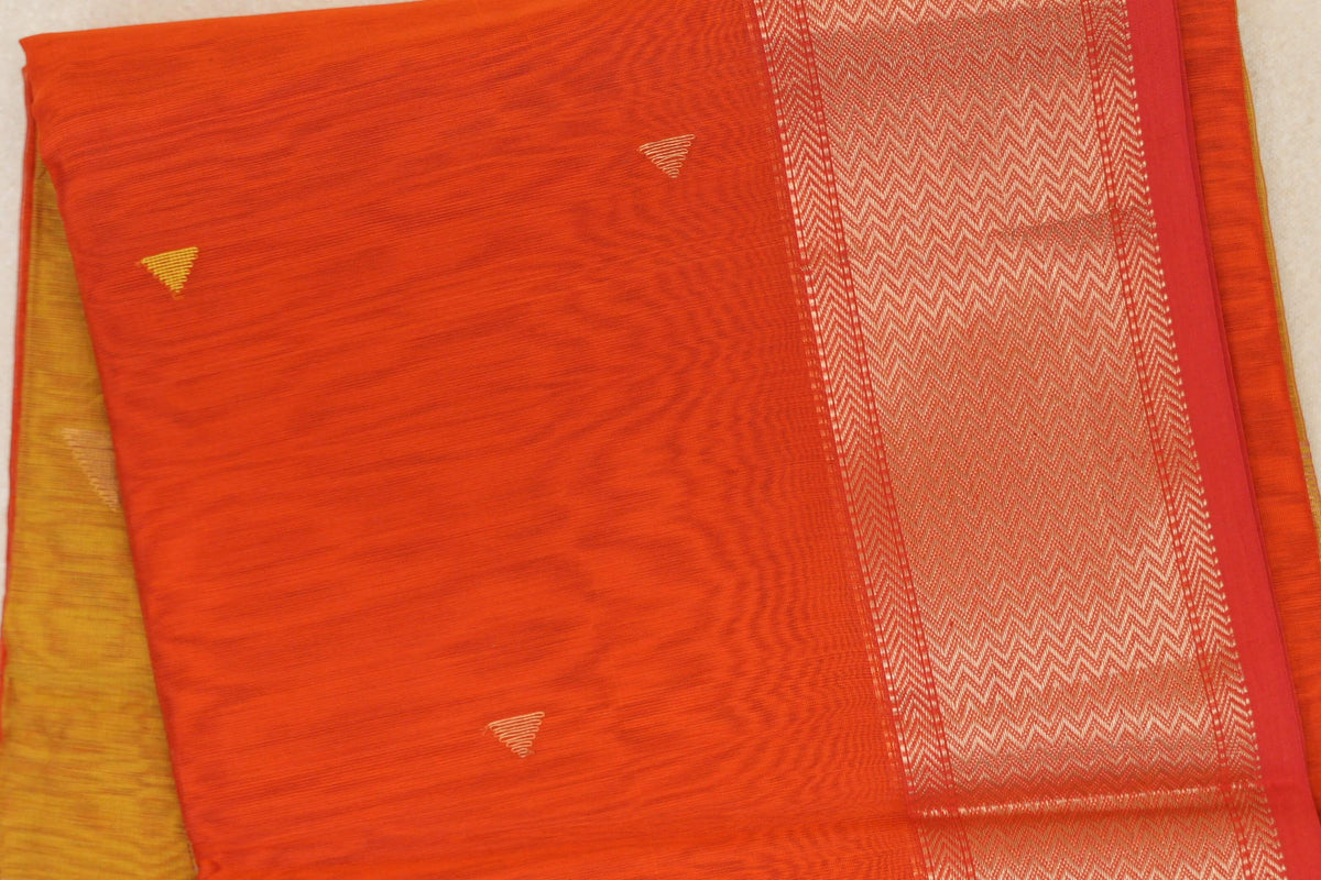 Folded Maheshwari silk cotton saree showing a reddish orange body with small gold-toned triangles and a broad orangish red zigzag border.