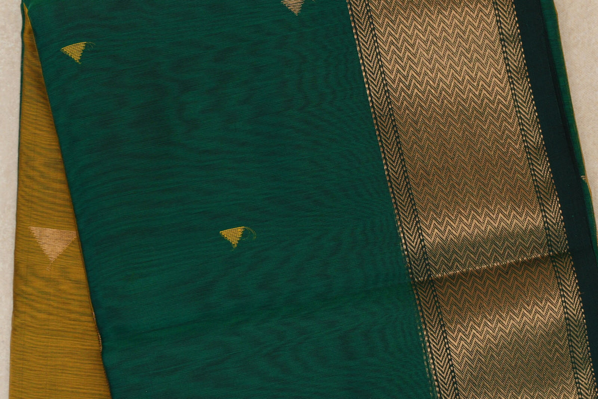 Close-up of a folded bottle green Maheshwari silk cotton saree with small gold motifs, a broad gold-patterned border and mustard yellow fabric beneath.