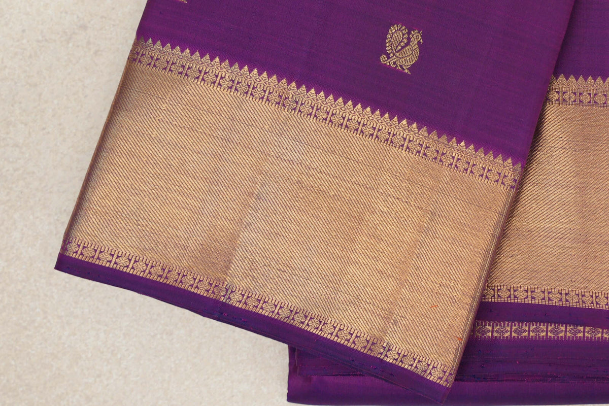 Folded purple Kanjivaram silk saree showing a gold paisley motif and a broad gold zari border with patterned purple edging.