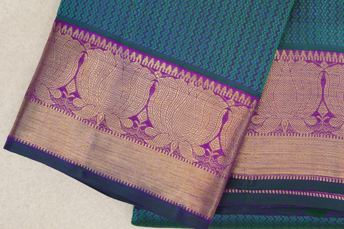 Folded peacock green Kanjivaram silk saree showing a geometric weave and wide purple border with gold woven patterns and bottle green selvedge.