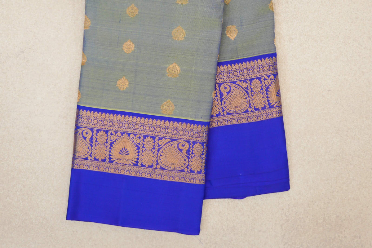 Folded yellowish green Kanchipuram silk saree with scattered gold leaf motifs and a royal blue border with gold paisley and floral patterns.