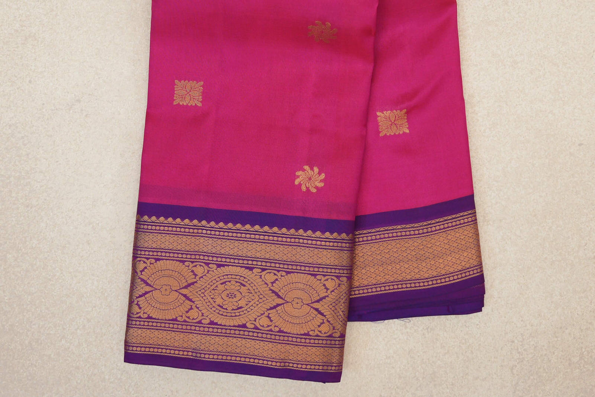 Folded rani pink Kanchipuram silk saree with scattered gold motifs and a magenta purple border woven with gold floral and geometric patterns.