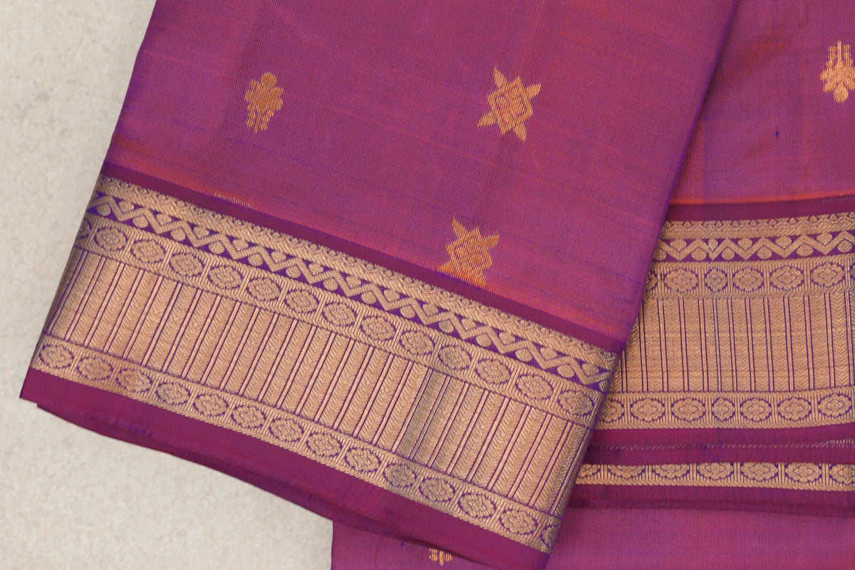 Folded blue and red Kanchipuram silk saree with scattered gold motifs and a wide border of geometric bands and floral medallions.