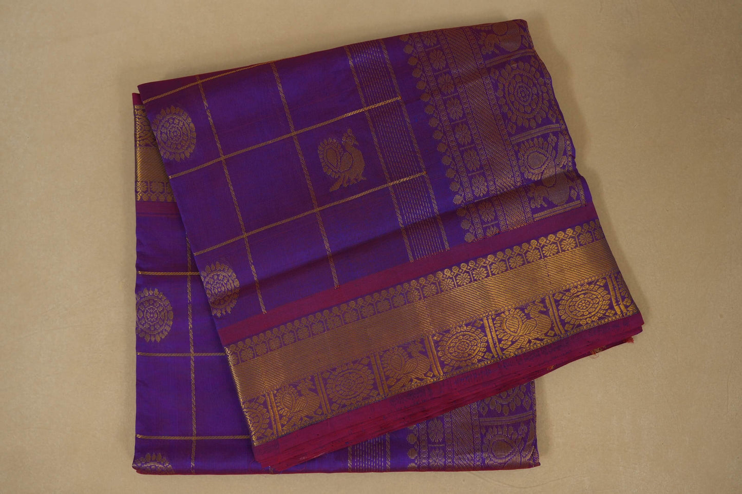 Purple and gold traditional saree with intricate patterns on a beige background, silk cotton , nine and a half yards saree, folded