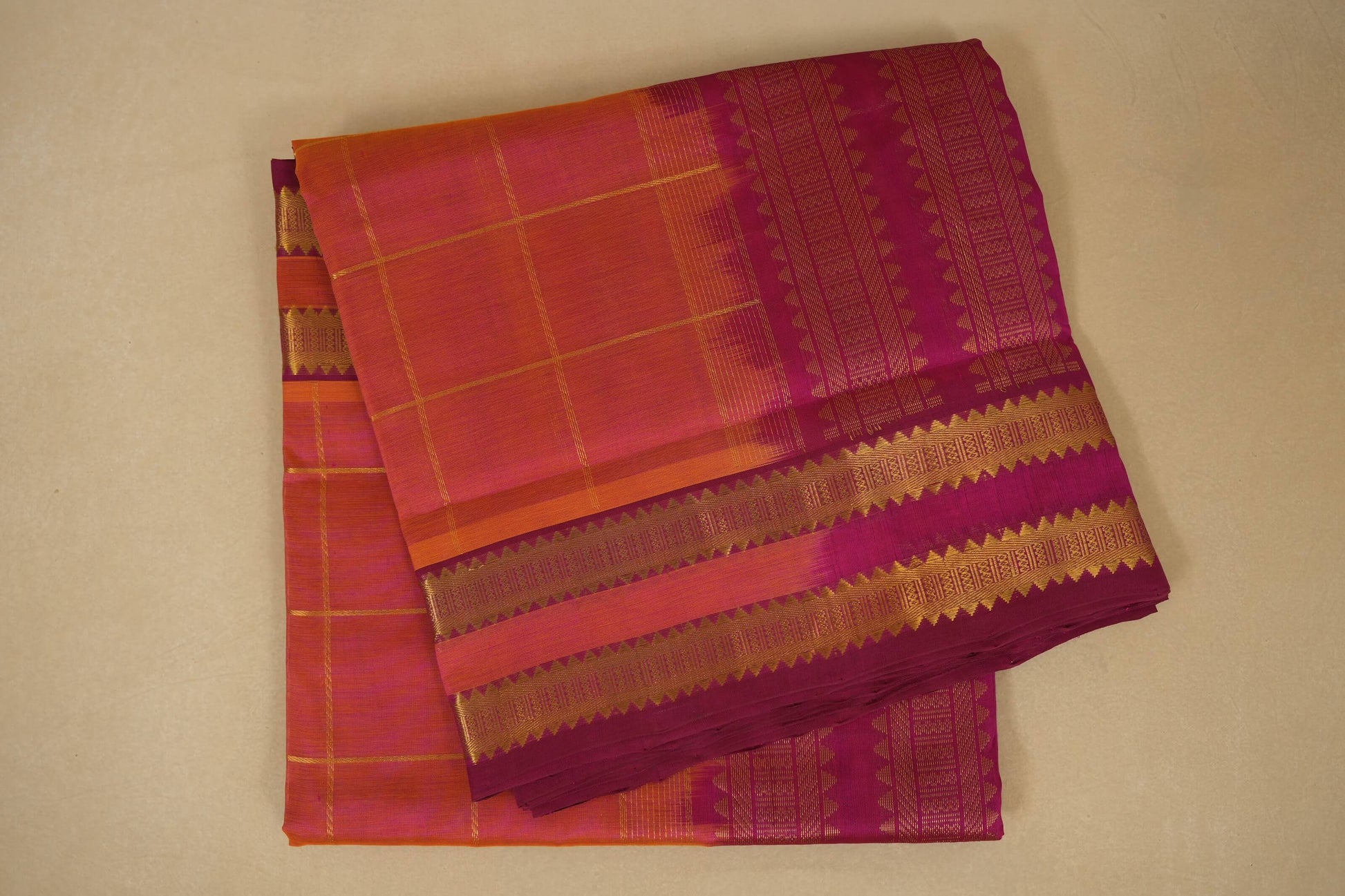 Folded traditional fabric with orange and pink checkered pattern on a beige background, silk cotton , nine and a half yards saree, folded