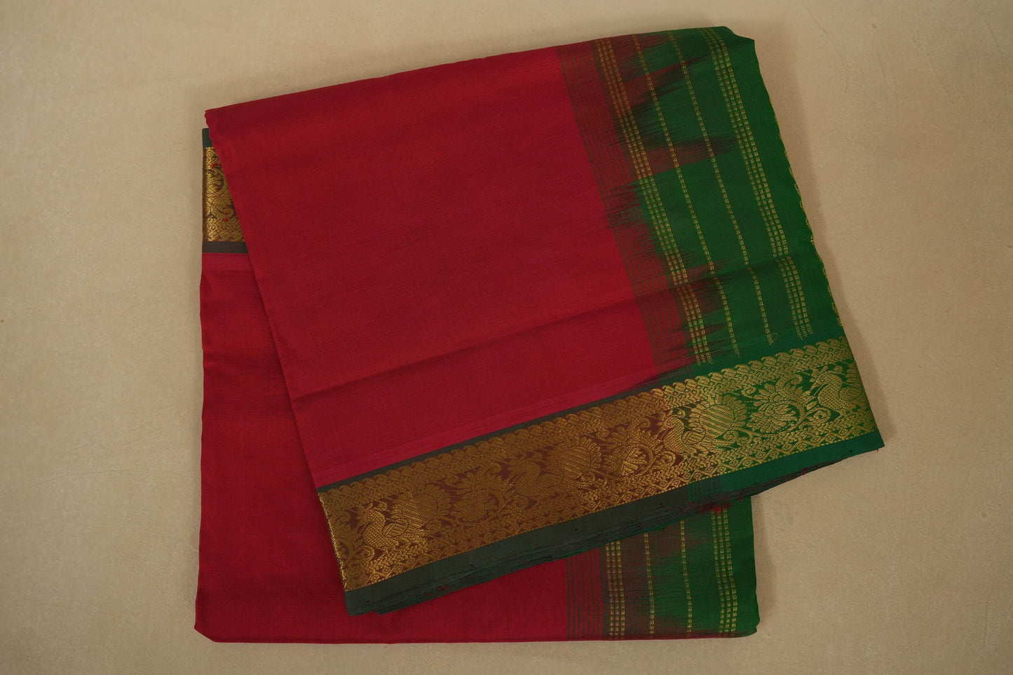 Red saree with green and gold border on a beige background, silk cotton , nine and a half yards saree folded