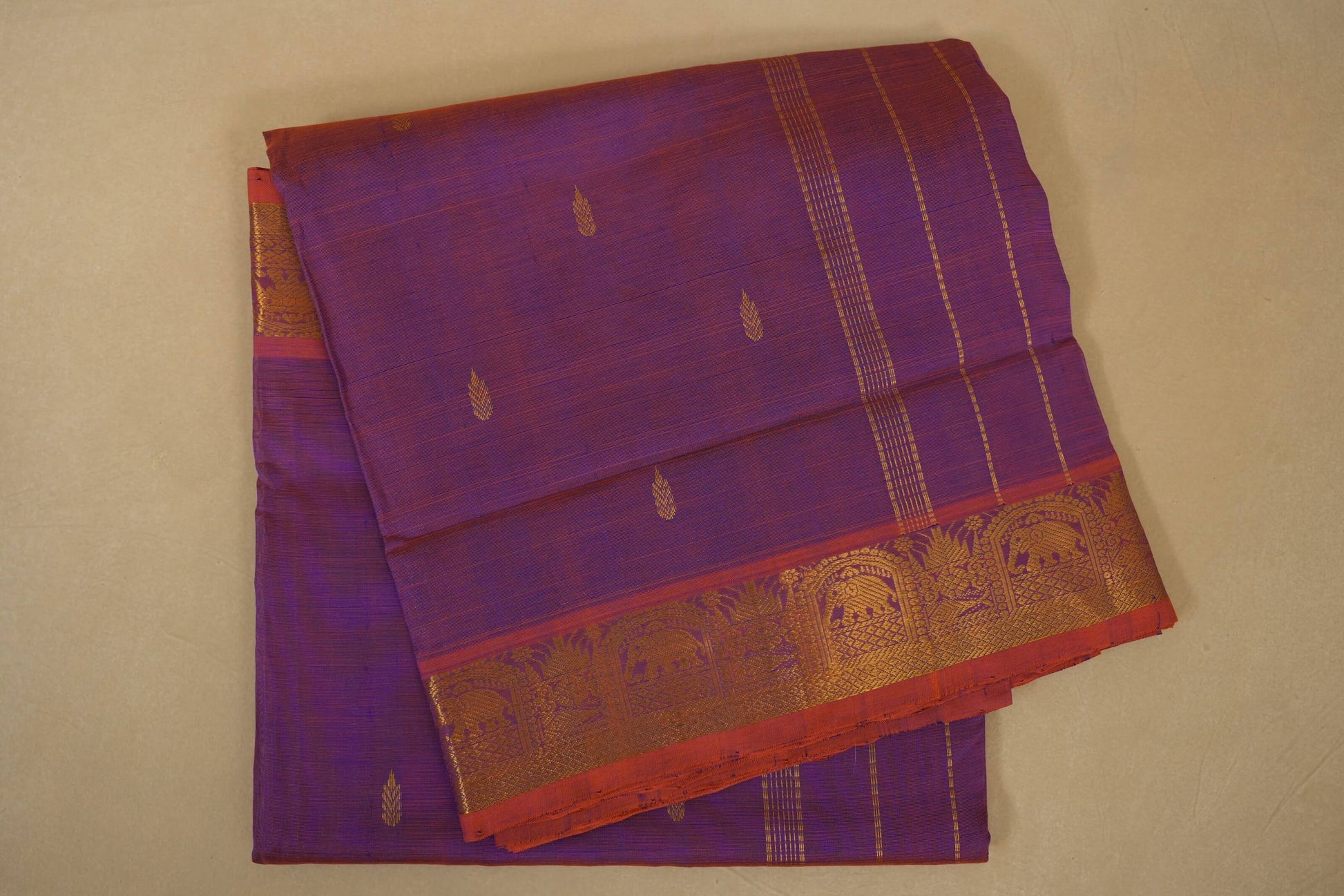 Purple saree with gold and red border on a beige background folded