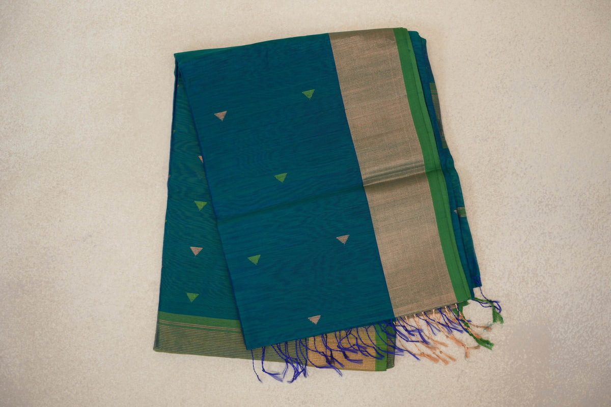 Folded peacock blue Maheshwari silk cotton saree with small green and gold triangles, a broad gold-toned border, parrot green edge and tassels.