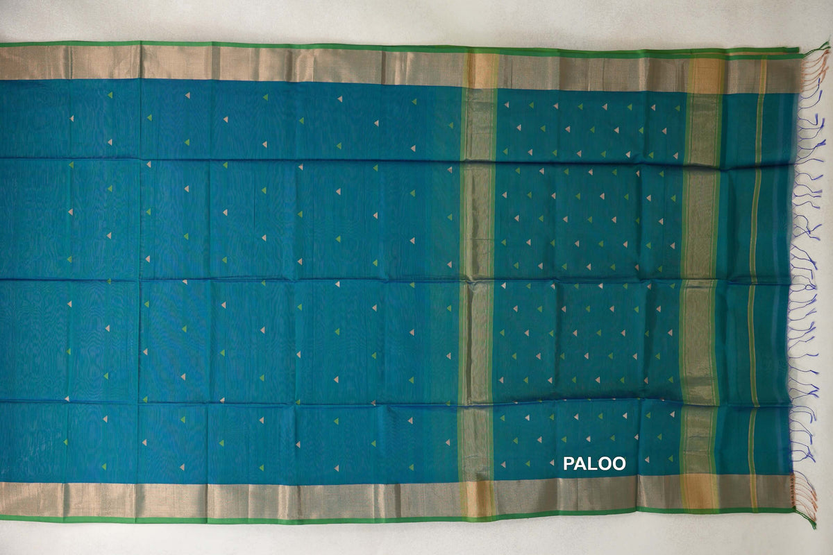 Peacock blue Maheshwari silk cotton saree laid flat, with small triangular motifs, broad borders with parrot green edges, and a striped pallu with tassels.