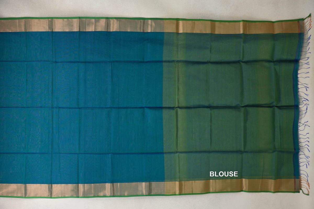 Maheshwari silk cotton saree laid flat, with a peacock blue body, parrot green blouse piece, broad gold-toned borders and tassels at one end.