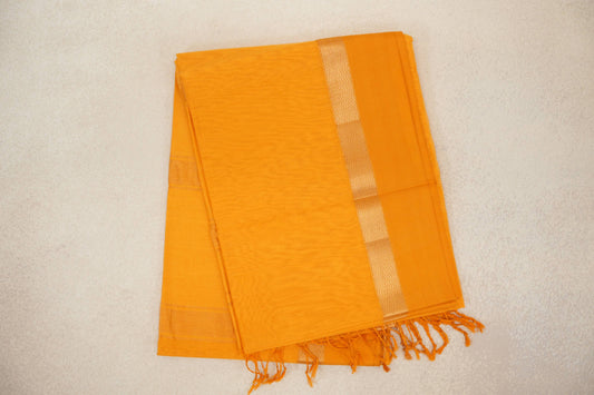 Folded mango yellow Maheshwari silk cotton saree with a pale zigzag border stripe and tassels along one edge.
