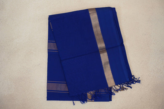 Folded deep royal blue Maheshwari silk cotton saree with a gold-toned zigzag border, fine stripes and blue tassels.