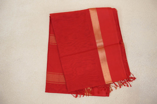 Folded Vermilion Red Maheshwari silk cotton saree with a subtle checked weave, gold zigzag border, fine stripes and red tassels.