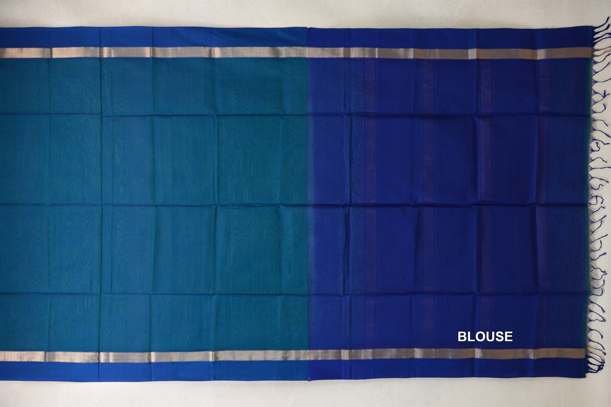 Maheshwari silk cotton saree laid flat, showing a peacock blue body beside a deep blue blouse piece, with narrow patterned borders and tassels.