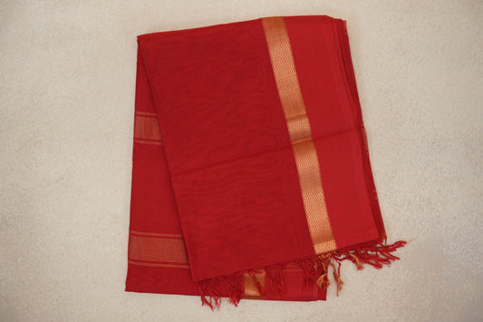 Folded vermilion red Maheshwari silk cotton saree with a fine checked weave, gold zigzag border, narrow stripes and red tassels.