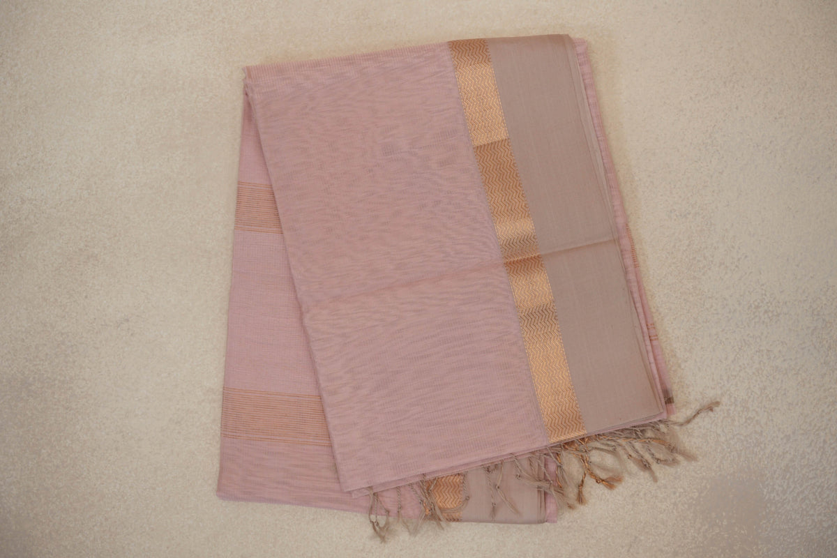 Folded blush pink Maheshwari silk cotton saree with a light sandal beige border, zigzag woven band and tassels along the edge.