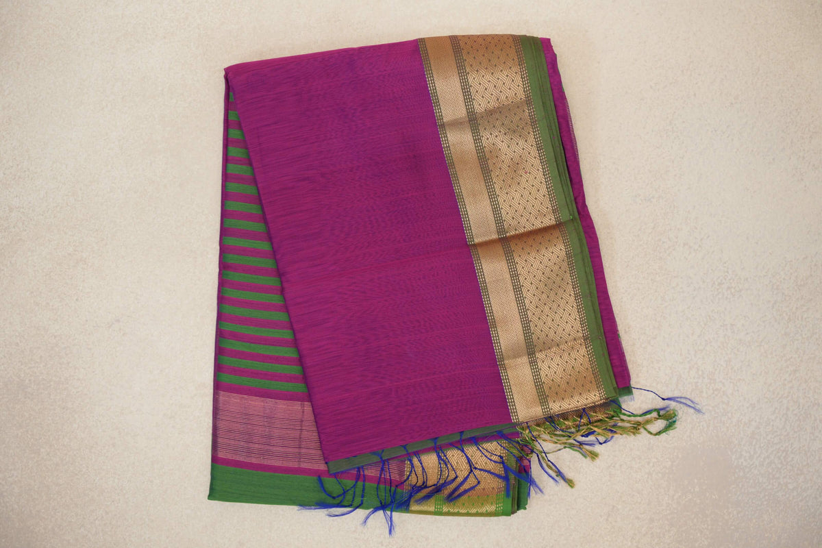 Folded dark magenta Maheshwari silk cotton saree with leaf green stripes, a patterned gold border and blue and green tassels.