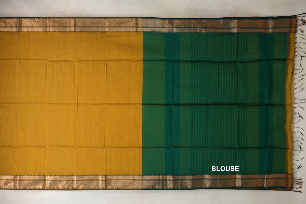 Maheshwari silk cotton saree laid flat, showing a mustard yellow body, gold-patterned borders and a deep emerald green blouse piece with fine stripes and tassels.