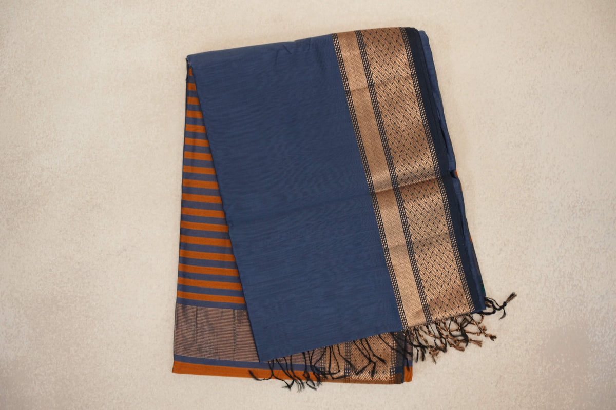 Folded dark grey blue Maheshwari silk cotton saree with a patterned border, deep orange pallu stripes and dark tassels.