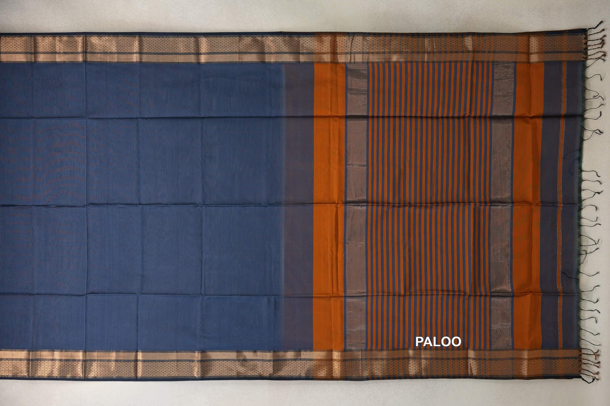 Maheshwari silk cotton saree spread flat, showing a dark grey blue body, patterned borders and a pallu with deep orange stripes and tassels.