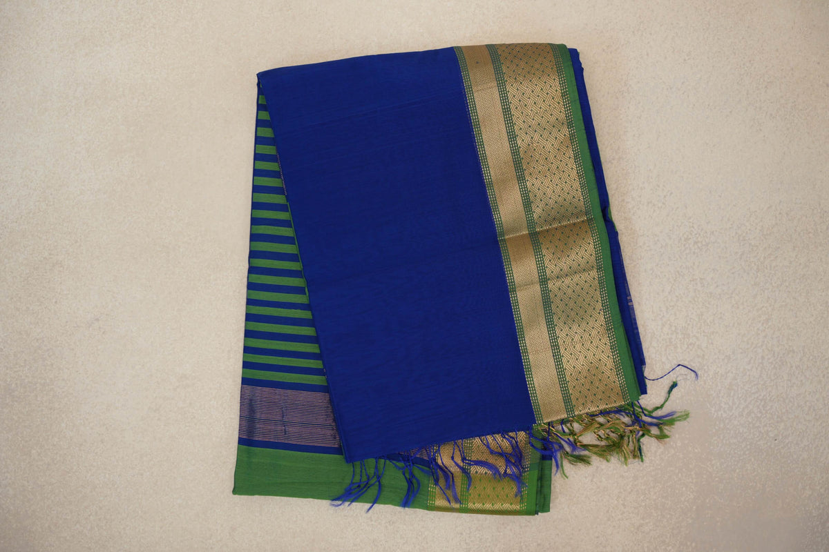Folded Maheshwari silk cotton saree with a bright royal blue body, leaf green and gold patterned border, striped pallu and tassels.