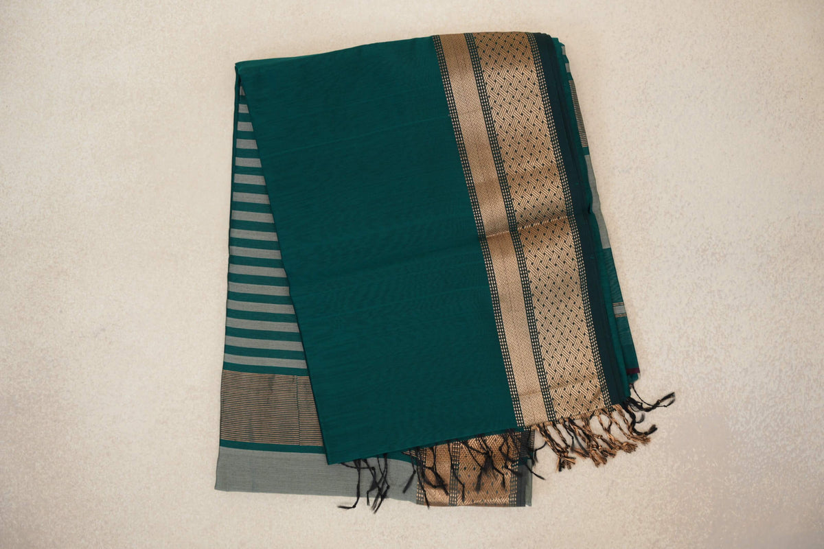 Folded peacock green Maheshwari silk cotton saree with silver grey stripes, a gold-toned geometric border and tassels.