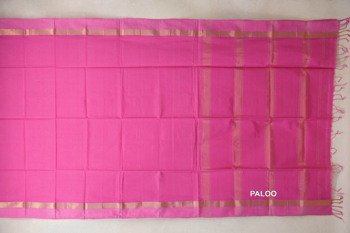 Bright rani pink Maheshwari silk cotton saree laid flat, showing a plain body, pink borders with gold-toned bands, and a striped pallu with tassels.