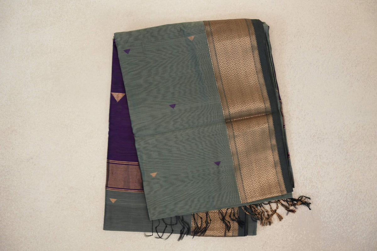 Folded sage green Maheshwari silk cotton saree with small triangle motifs, a dark sage border with gold chevrons, and a visible deep purple panel.