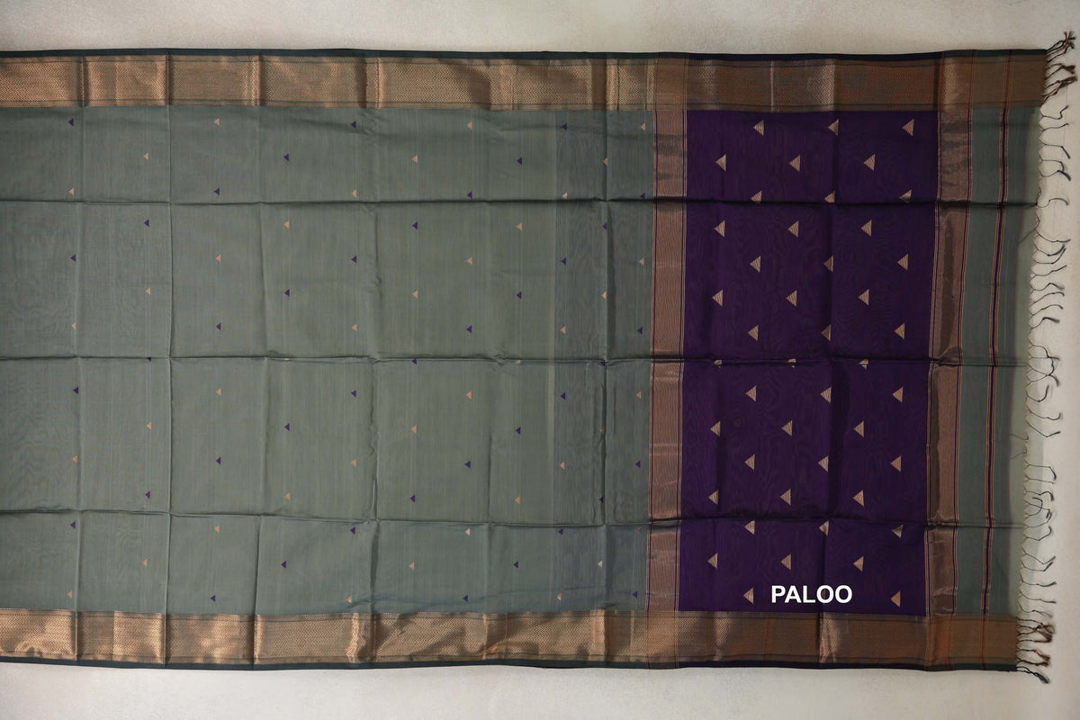Maheshwari silk cotton saree laid flat, with a sage green body dotted with small triangles, patterned dark sage green borders and a deep purple pallu.
