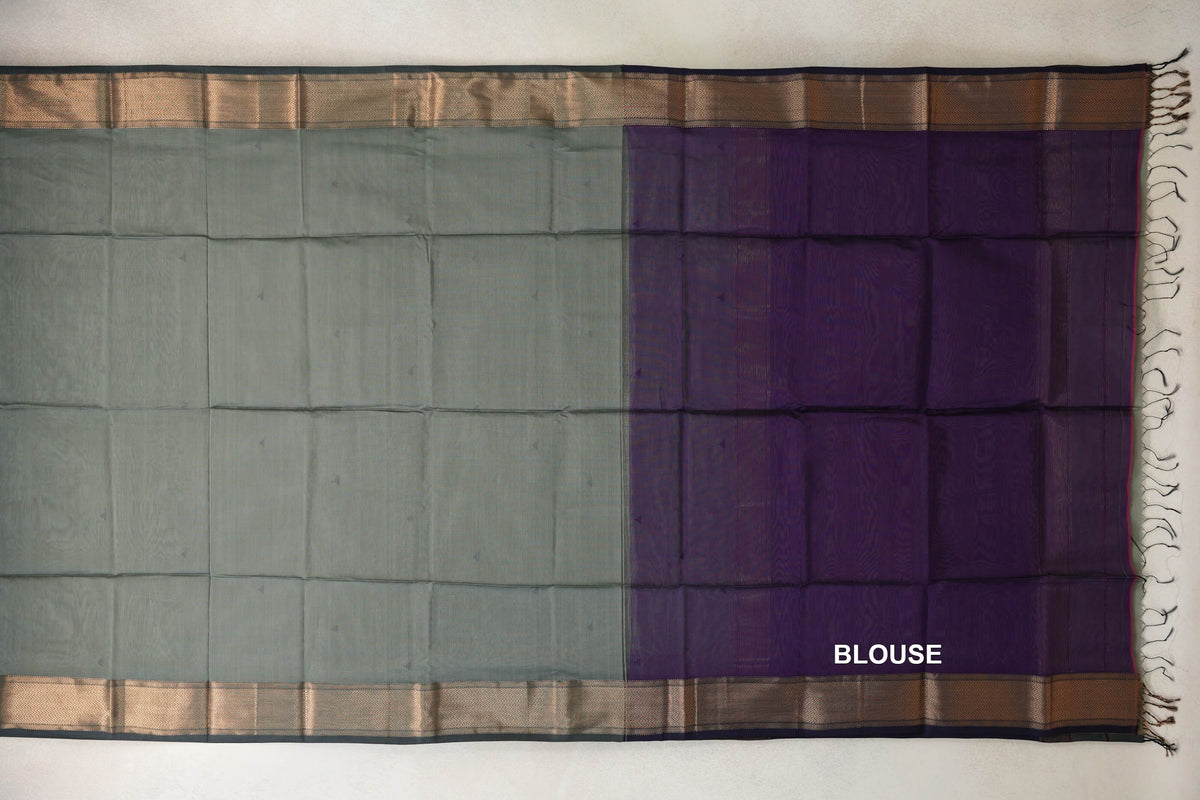 Maheshwari silk cotton saree laid flat, showing a sage green body, deep purple blouse piece, patterned borders and tassels at one end.