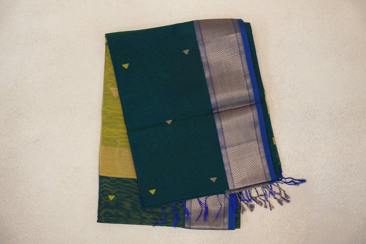 Folded Maheshwari silk cotton saree with a peacock green body, small triangle motifs, and a chevron-patterned border edged in royal blue with tassels.