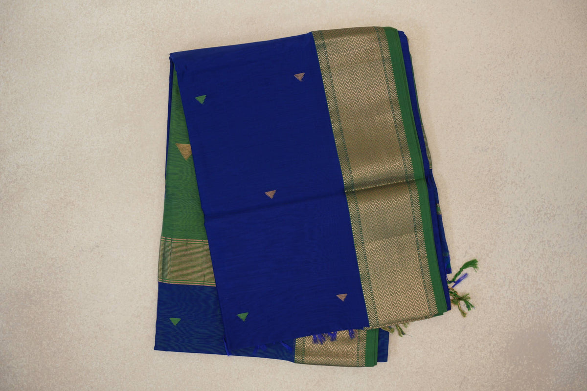 Folded Maheshwari silk cotton saree with a royal blue body, small triangle motifs, a leaf green border with gold chevrons, and tassels.