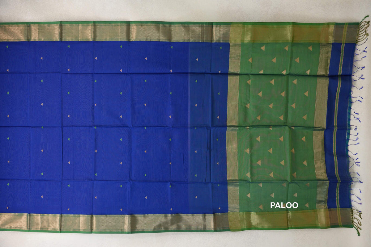 Maheshwari silk cotton saree spread flat, with a royal blue body dotted with small triangles, a leaf green pallu, patterned borders and tassels.