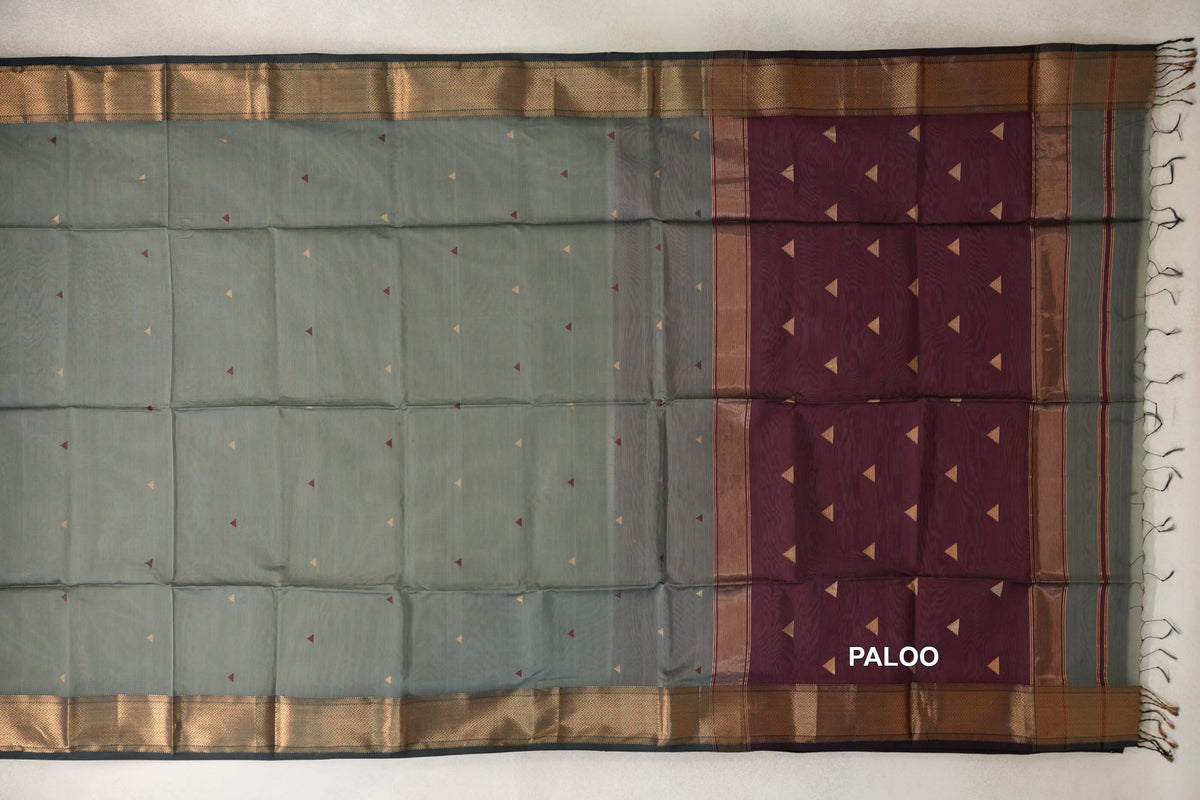 Maheshwari silk cotton saree laid flat, showing a sage green body with small triangle motifs, patterned dark sage green borders and a deep wine maroon pallu.