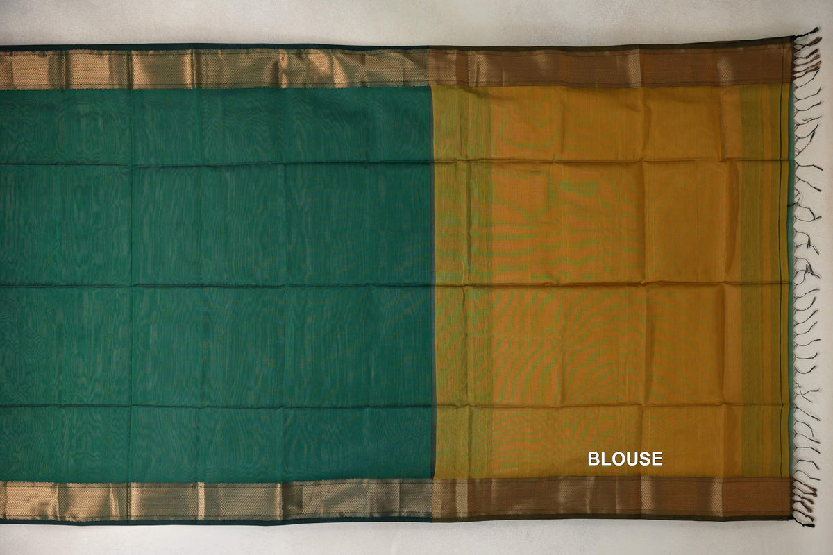Maheshwari silk cotton saree laid flat, showing a bottle green body, mustard yellow blouse piece, patterned gold-toned borders and dark tassels.