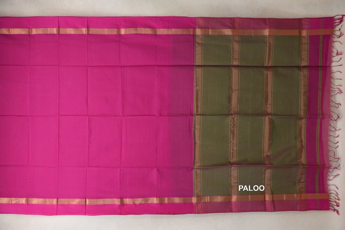 Maheshwari silk cotton saree laid flat, showing a plain rani pink body, gold-toned border bands and an olive green striped pallu with tassels.
