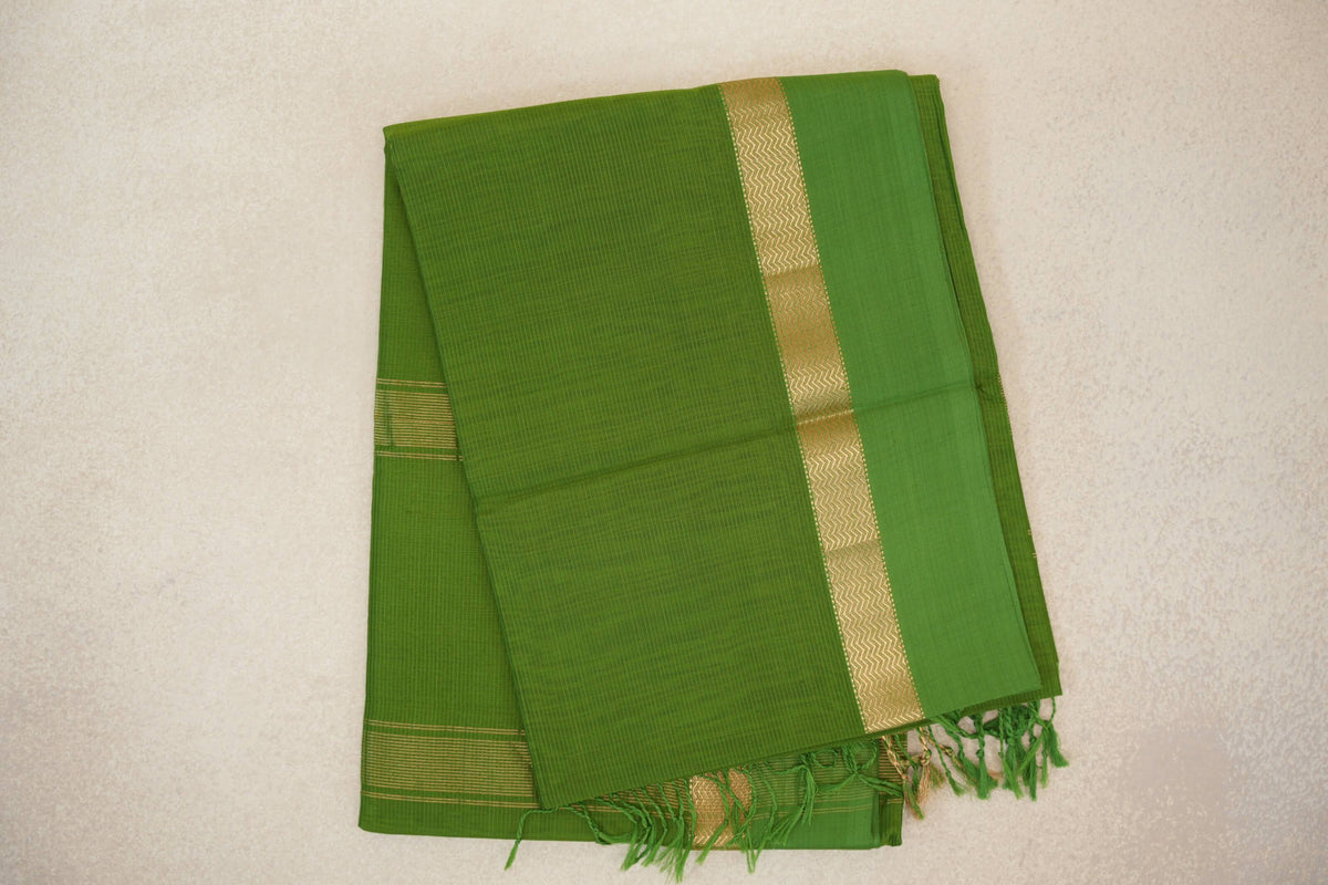 Folded leaf green Maheshwari silk cotton saree with fine checked lines, a gold-tone zigzag border and green tassels.