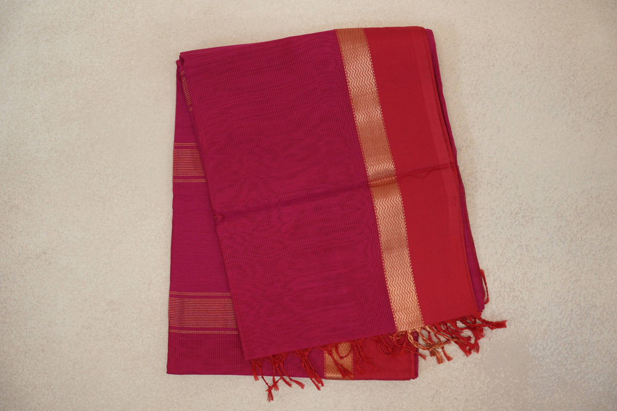 Folded bright rani pink Maheshwari silk cotton saree with a deep rani pink border, gold-toned zigzag stripe and tassels.