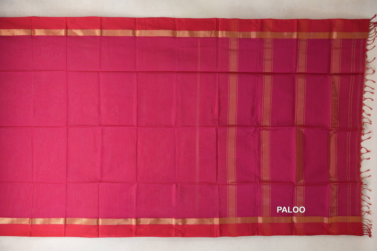 Maheshwari silk cotton saree laid flat, with a bright rani pink body, deep rani pink borders, and a striped pallu with gold-toned bands and tassels.