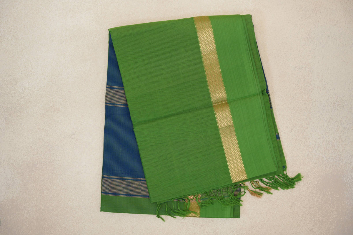 Folded bright leaf green Maheshwari silk cotton saree with a gold zigzag band, a peacock blue striped section and green tassels.