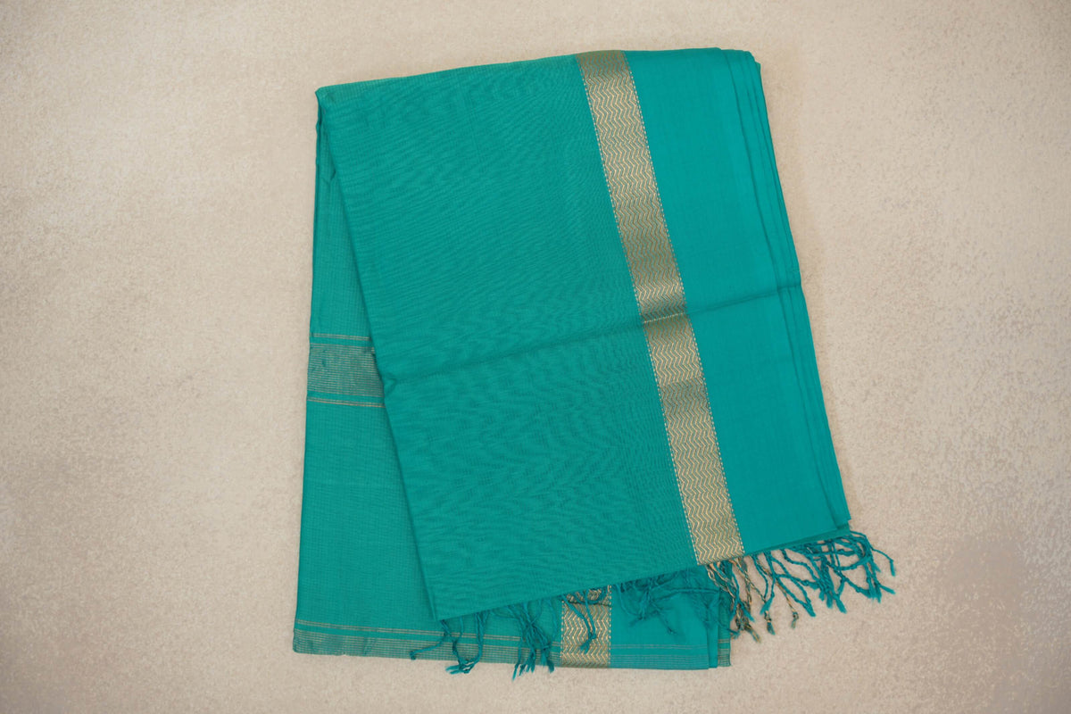 Folded bright aqua green Maheshwari silk cotton saree with a gold-toned zigzag border, fine stripes and tasseled ends.