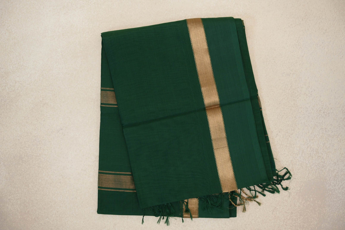 Folded deep bottle green Maheshwari silk cotton saree with a gold-toned woven border, fine striped accents and green tassels.