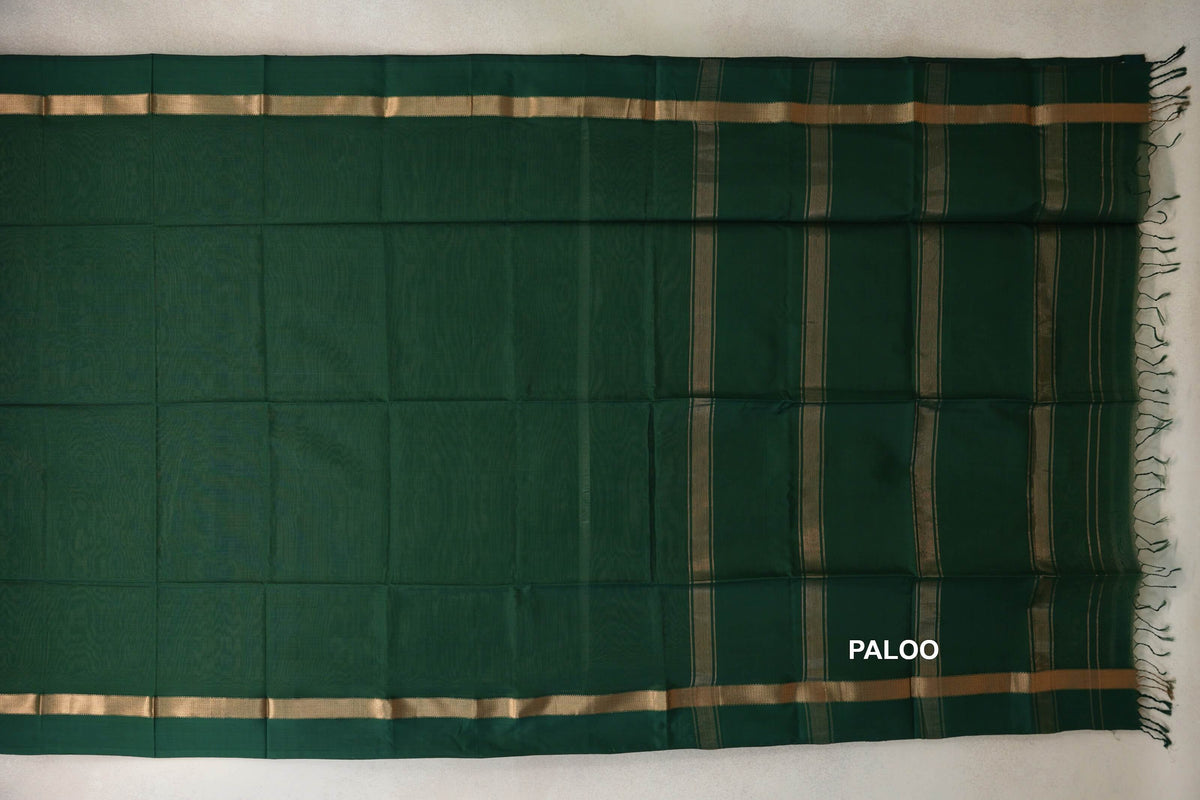 Deep bottle green Maheshwari silk cotton saree laid flat, with gold-toned borders and a striped pallu ending in tassels.
