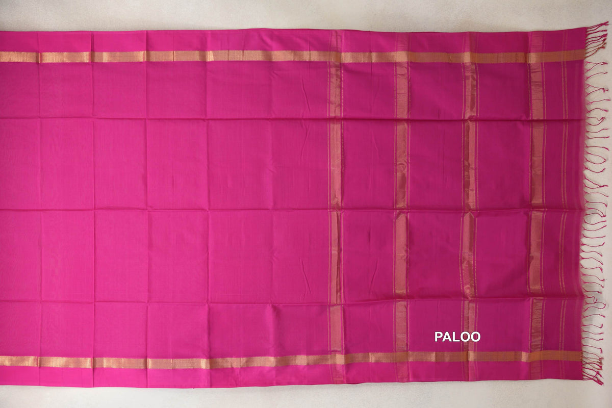 Maheshwari silk cotton saree spread flat, showing a bright rani pink body, pink borders with gold-toned bands, and a striped pallu with tassels.