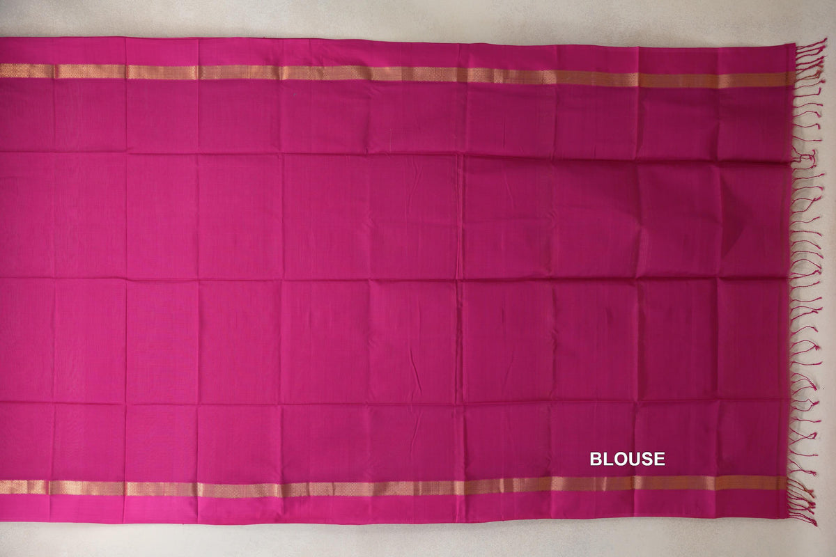 Bright rani pink Maheshwari silk cotton blouse piece laid flat, with narrow gold-toned bands along the top and bottom and pink tassels at one end.